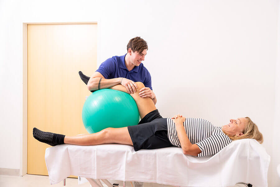 Physiotherapie-Sitzung: Therapeut unterstützt Patientin mit einem Gymnastikball.