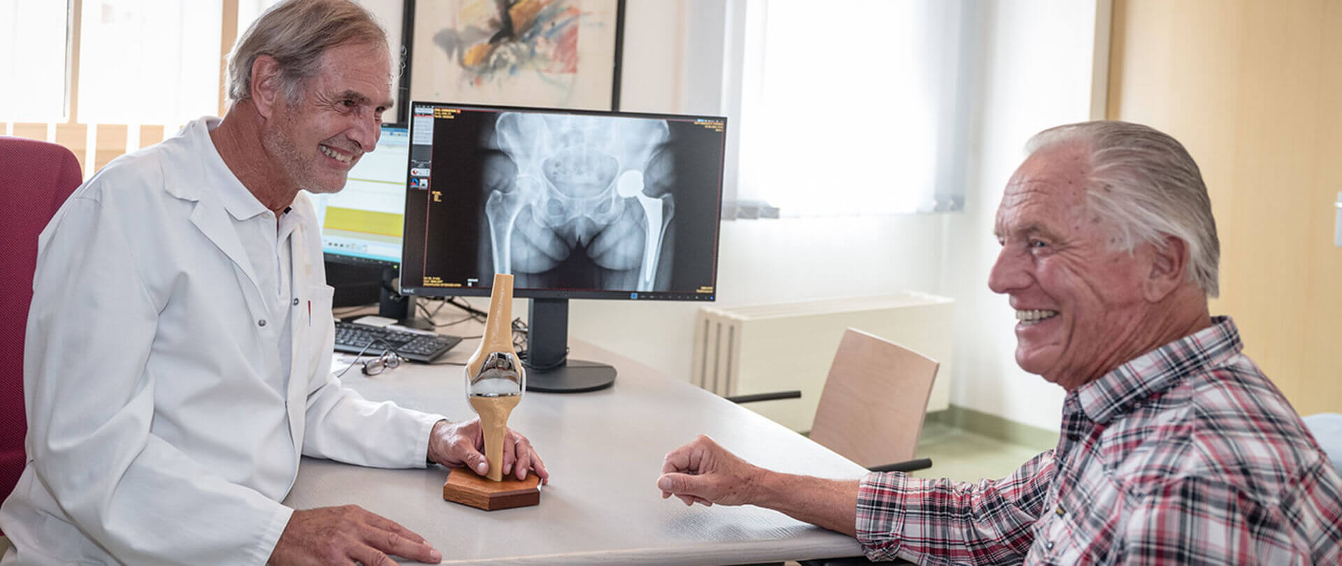 Arztgespräch mit lächelndem Patienten, Röntgenbild im Hintergrund, in moderner Praxis.