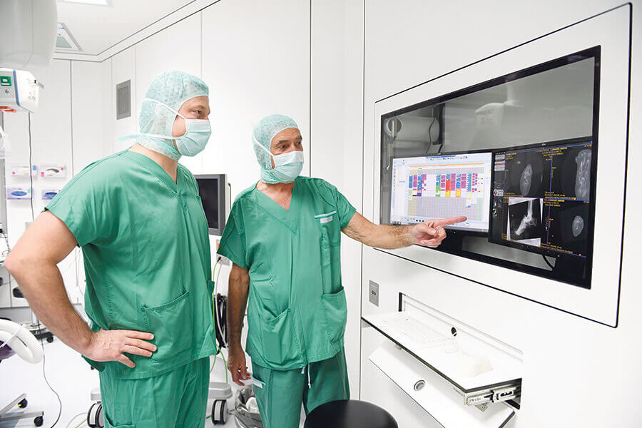 Ärzte in OP-Kleidung betrachten medizinische Bilder an einem Bildschirm in der Privatklinik.