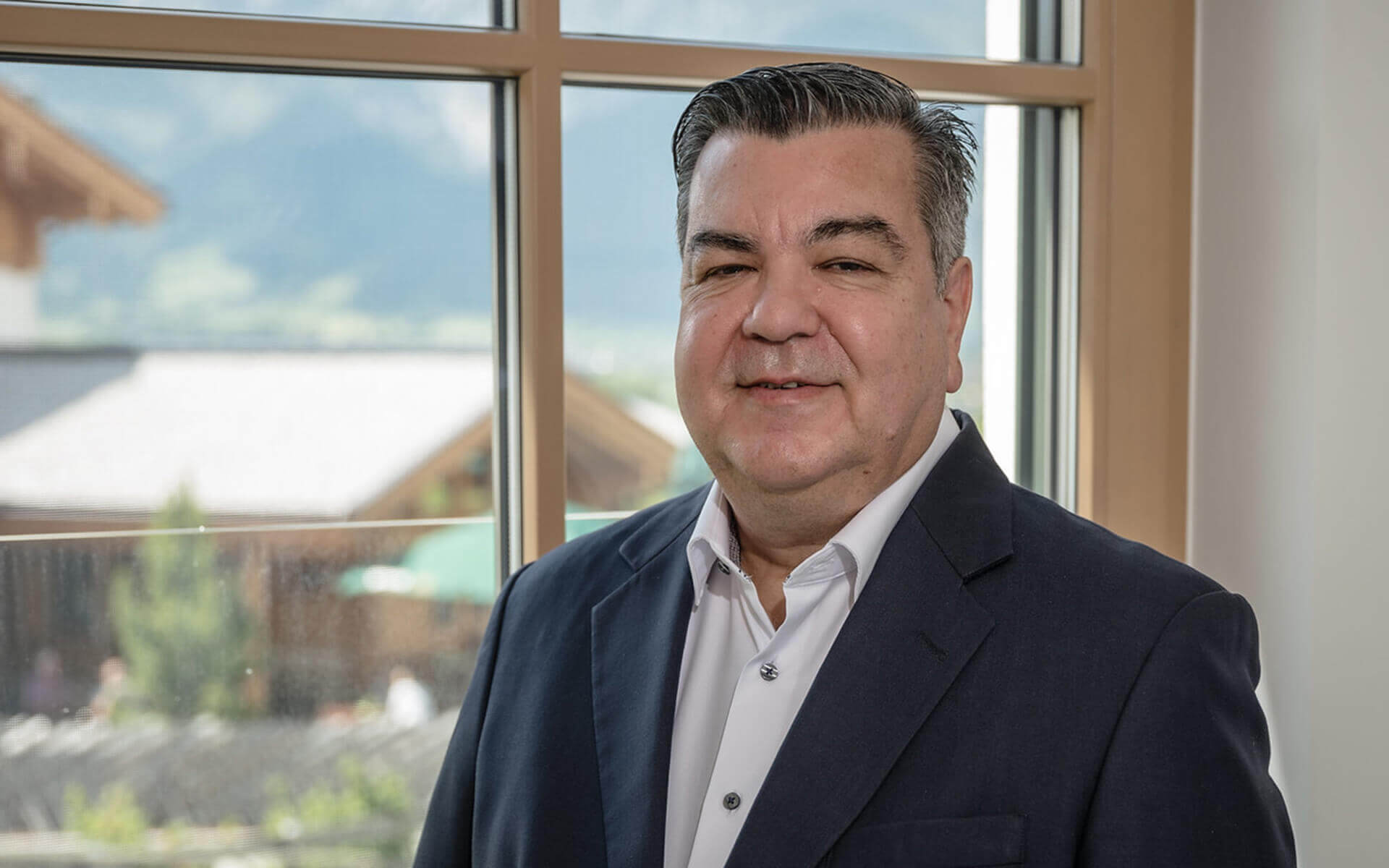 Mann in Anzug vor Fenster, Blick auf das malerische Salzburger Land, Privatklinik-Umgebung.
