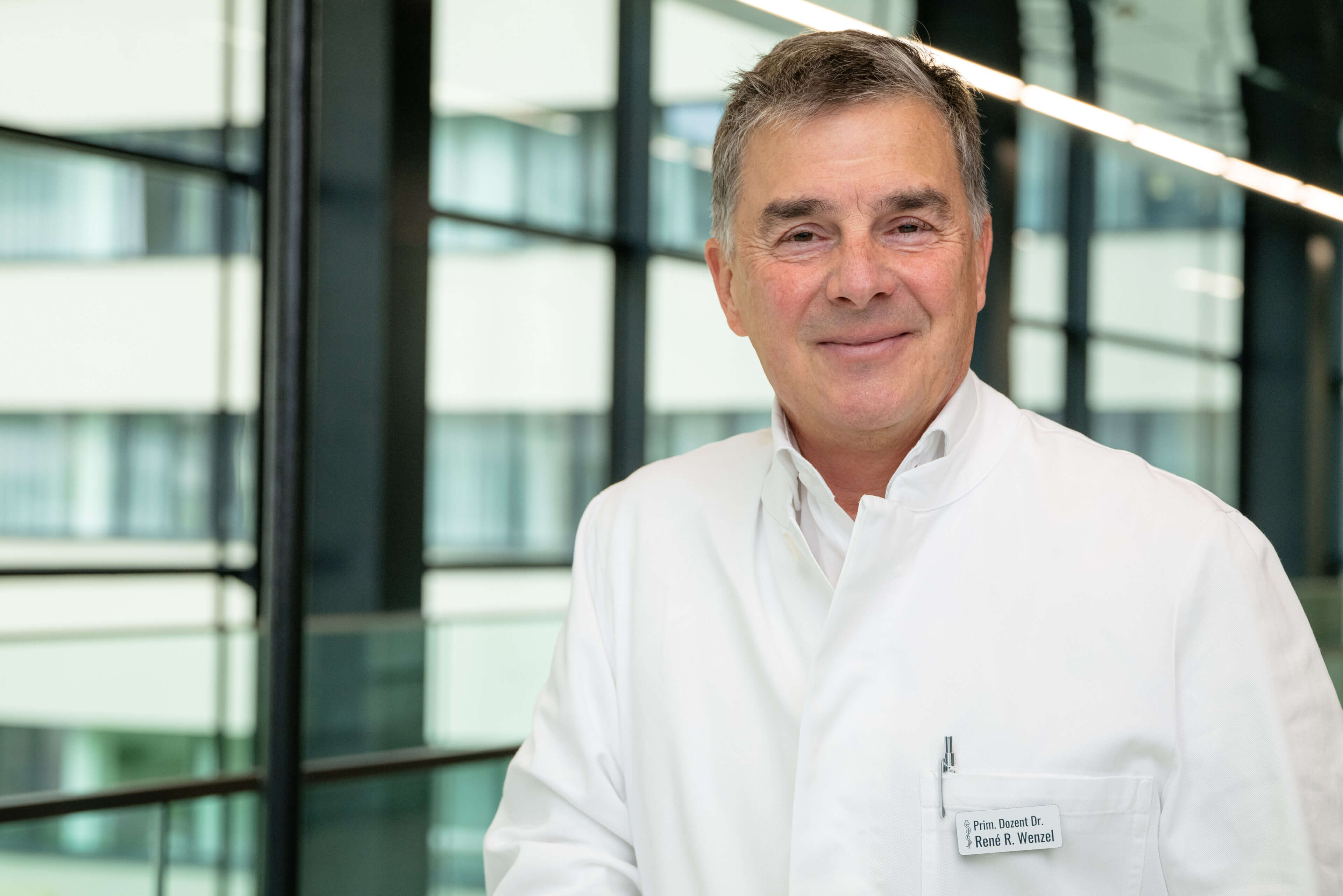 Facharzt in weißem Kittel lächelt im modernen Umfeld der Privatklinik Ritzensee.