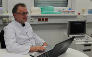 Dr. Peter Metzger in der Klinik, arbeitet am Laptop in moderner Behandlungsumgebung.
