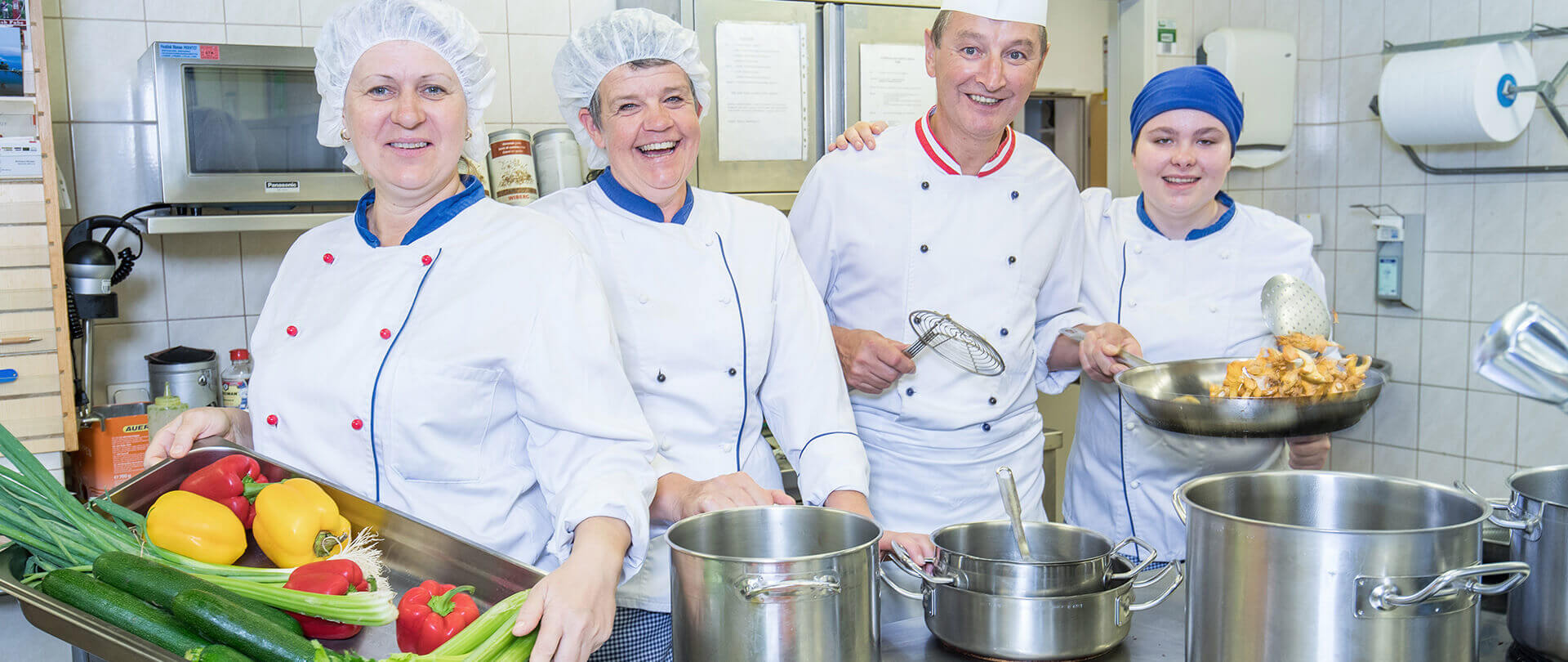Köche in der Klinikküche präsentieren frisches Gemüse und Küchengeräte für gesunde Ernährung.